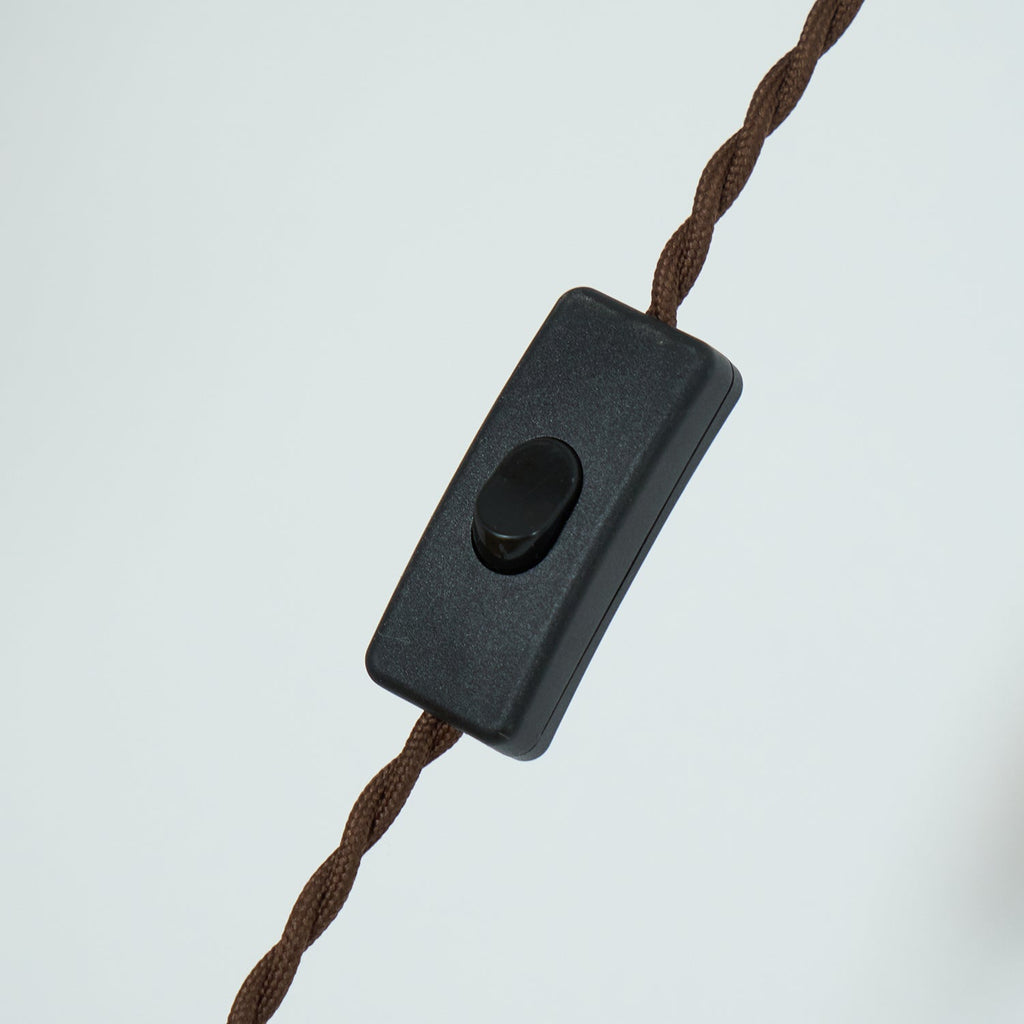 The inline black rocker switch on the twisted brown fabric cord of the Clérachic plug-in amber glass pendant light.