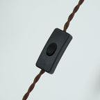 The inline black rocker switch on the twisted brown fabric cord of the Clérachic plug-in amber glass pendant light.