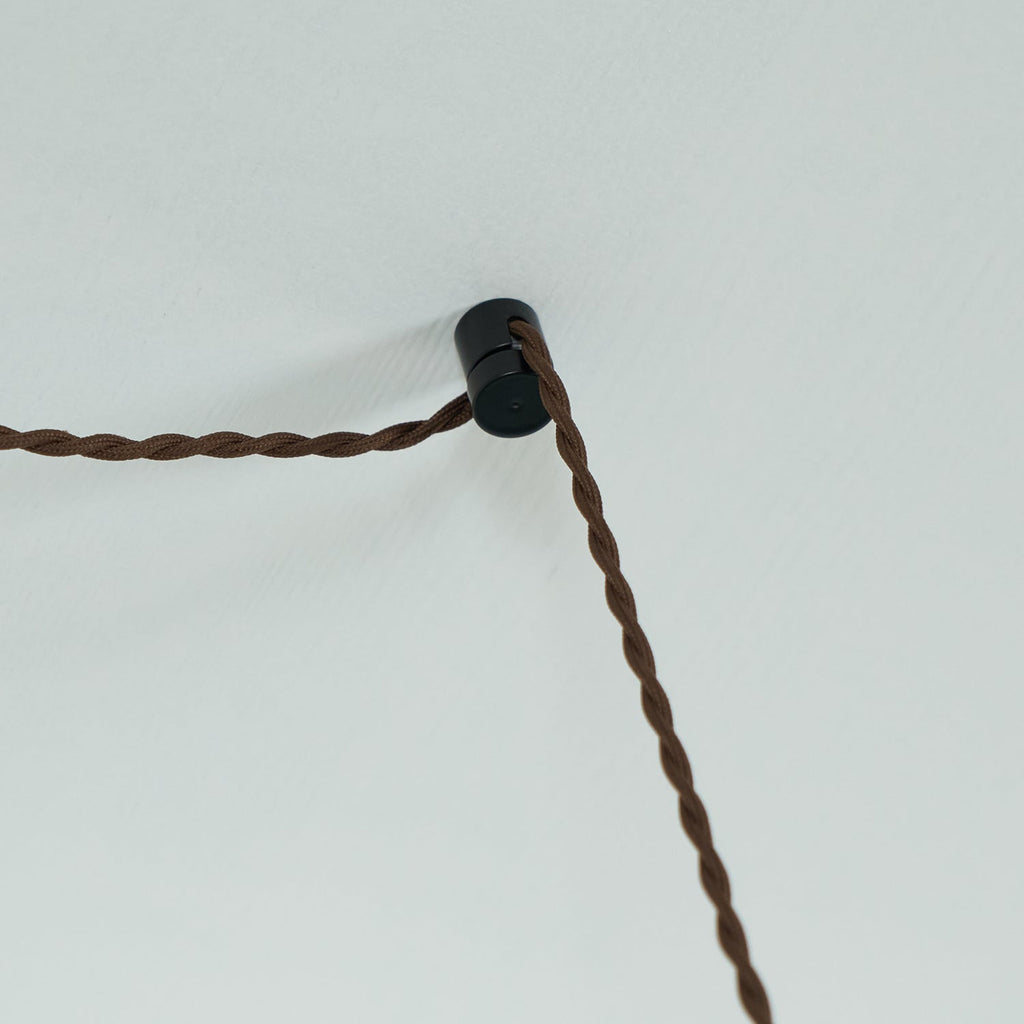The small black cord hook that carries the twisted fabric flex of a Clérachic plug-in amber glass pendant across the ceiling.