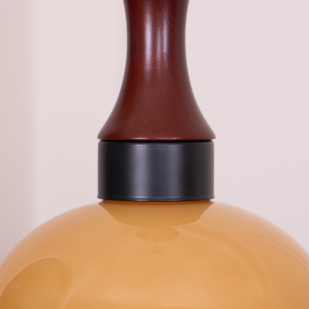 Close view where the walnut neck of a Clérachic amber glass pendant meets the matte black collar above the amber shade.