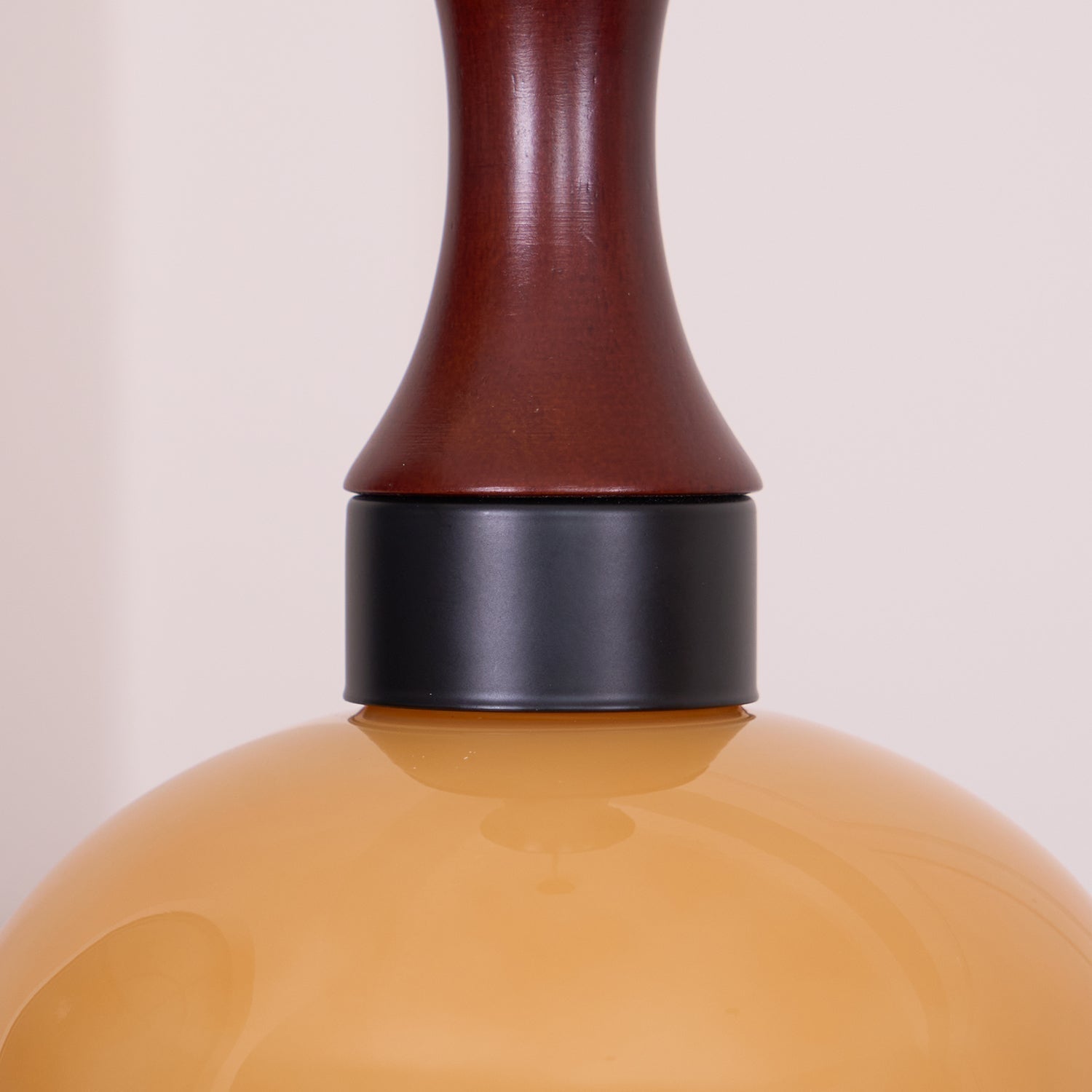 Close view where the walnut neck of a Clérachic amber glass pendant meets the matte black collar above the amber shade.