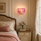 Lit pink disc wall light from Clérachic glowing beside a bed with a floral headboard, a pink throw and a bedside table with roses.