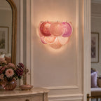 Pink swirled-glass wall light from Clérachic lit in a panelled hallway, with a vase of pink and burgundy flowers on a marble-topped console below.