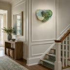 Blue and green glass-disc wall light from Clérachic on a panelled stairwell wall above a wooden console with baskets.