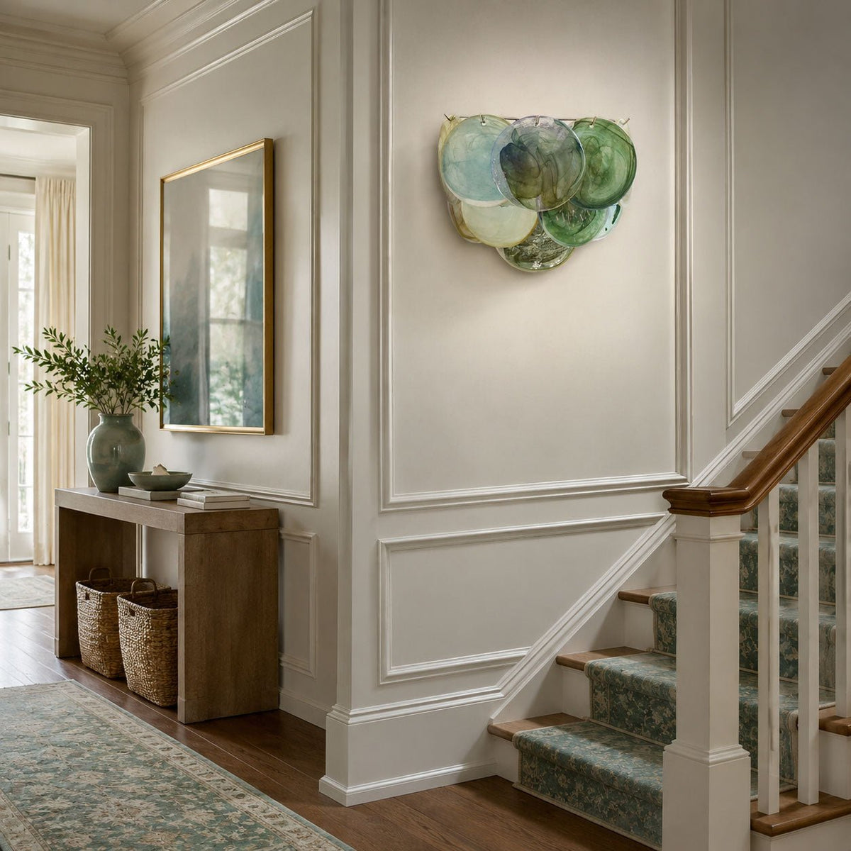 Blue and green glass-disc wall light from Clérachic on a panelled stairwell wall above a wooden console with baskets.