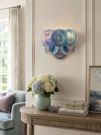 Blue and lilac disc wall light from Clérachic above a carved console table with pale hydrangeas in a green vase.