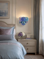 Small blue disc wall light from Clérachic glowing above a bedside table next to a bed dressed in blue and mauve linen.