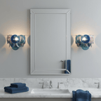 Pair of blue glass-disc wall lights from Clérachic flanking a framed mirror above a marble bathroom vanity with folded navy towels.