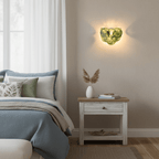 Green glass-disc wall light from Clérachic lit above a white bedside table and a bed with blue and sage bedding.