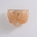 Unlit orange glass-disc wall light from Clérachic with swirled amber-peach discs layered in three tiers on a pale wall.