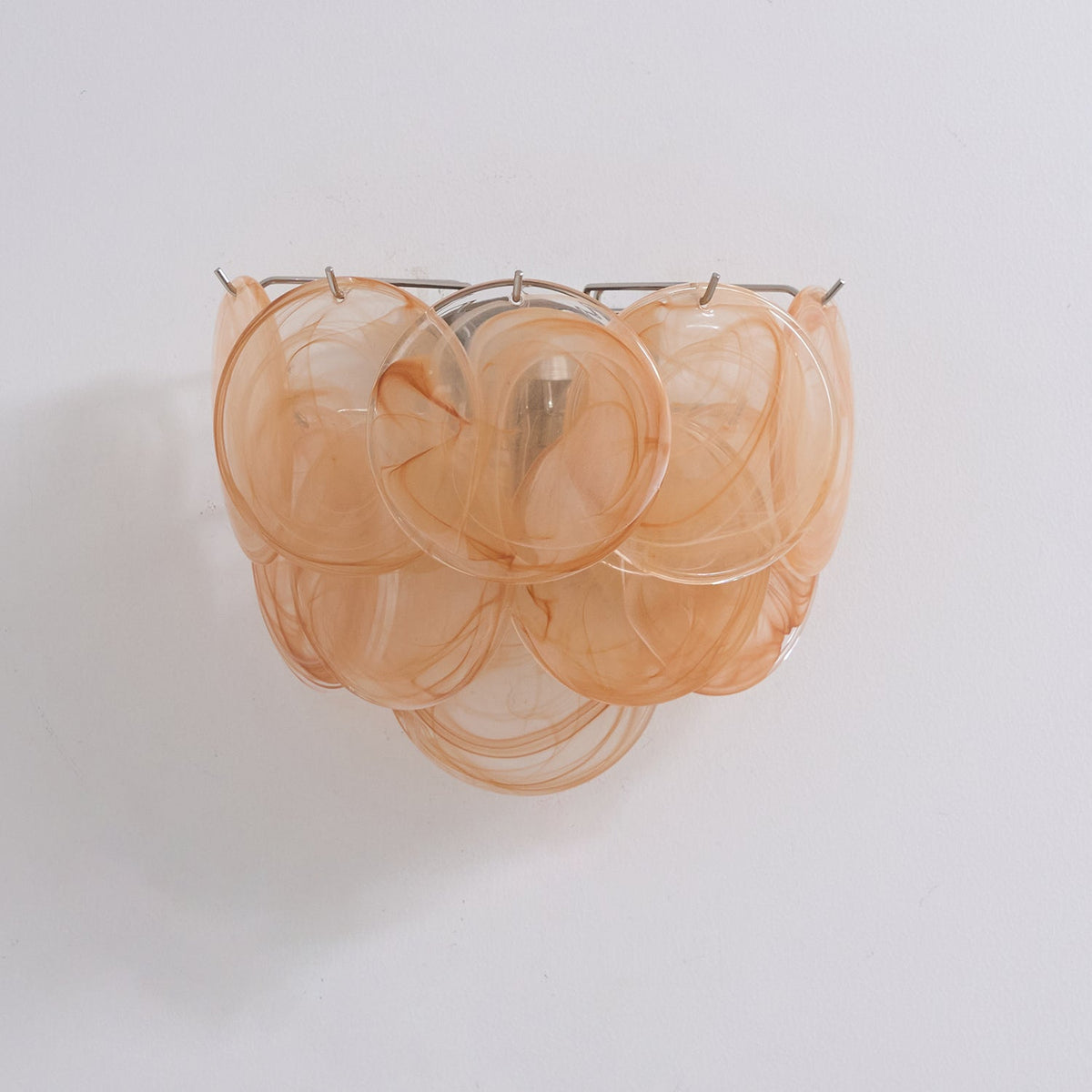 Unlit orange glass-disc wall light from Clérachic with swirled amber-peach discs layered in three tiers on a pale wall.