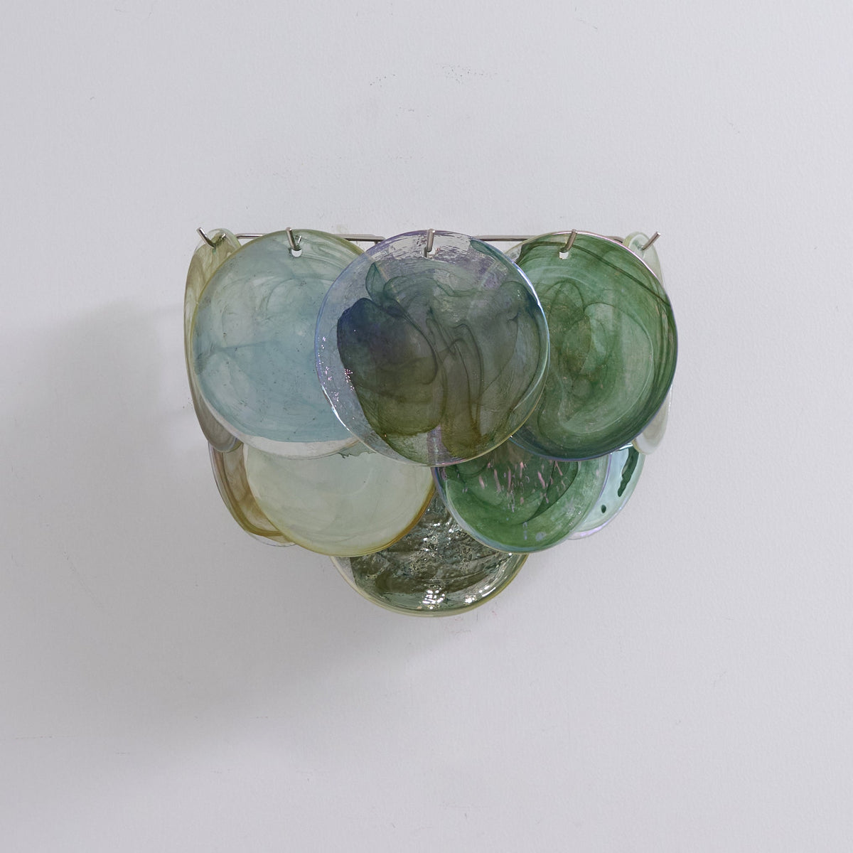 Unlit wall light from Clérachic with blue, green and cream swirled glass discs hung from slim metal pins on a pale wall.