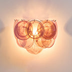 Orange glass-disc wall light from Clérachic lit, glowing warm with amber and rose swirls and a bright bulb behind the discs.