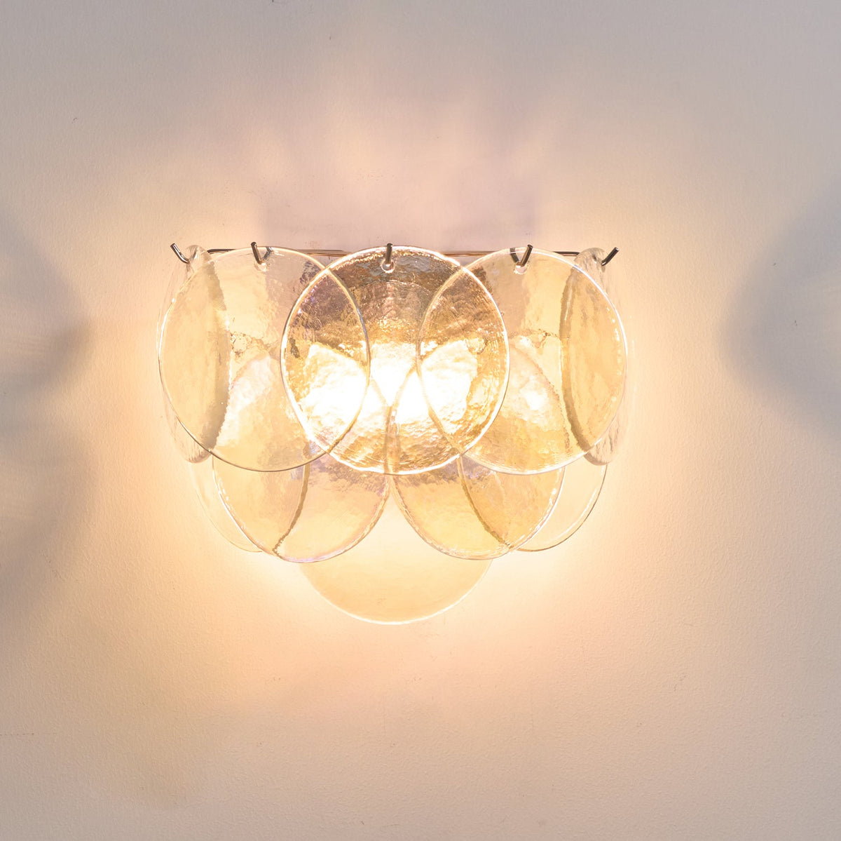 Clear glass-disc wall light from Clérachic lit, with textured discs glowing a soft warm white on a cream wall.