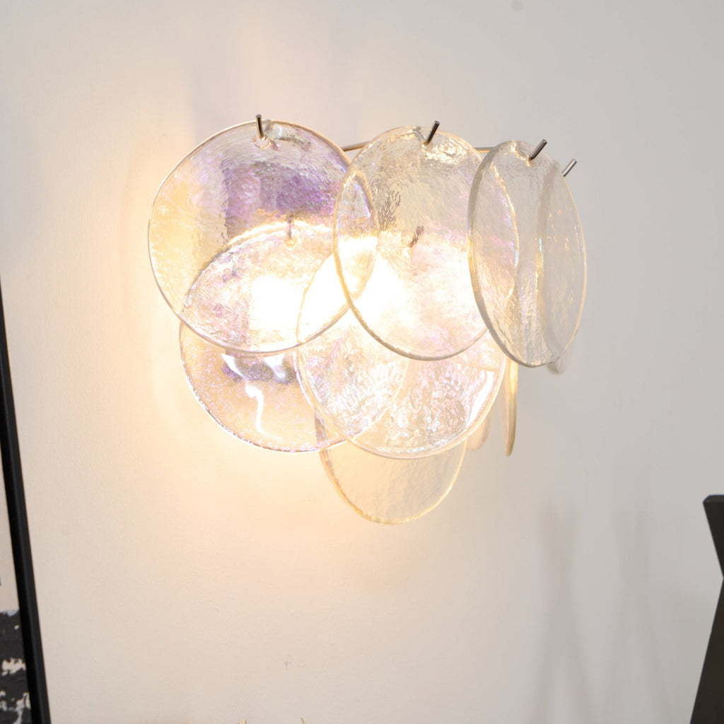 Close view of clear iridescent glass discs on this Clérachic wall light, lit from within with a faint purple sheen.