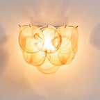Close view of orange swirled glass discs on this Clérachic wall light, glowing amber with the bulb visible through the glass.