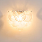 Close view of clear swirled glass discs on this Clérachic wall light, lit to a soft warm white against a cream wall.
