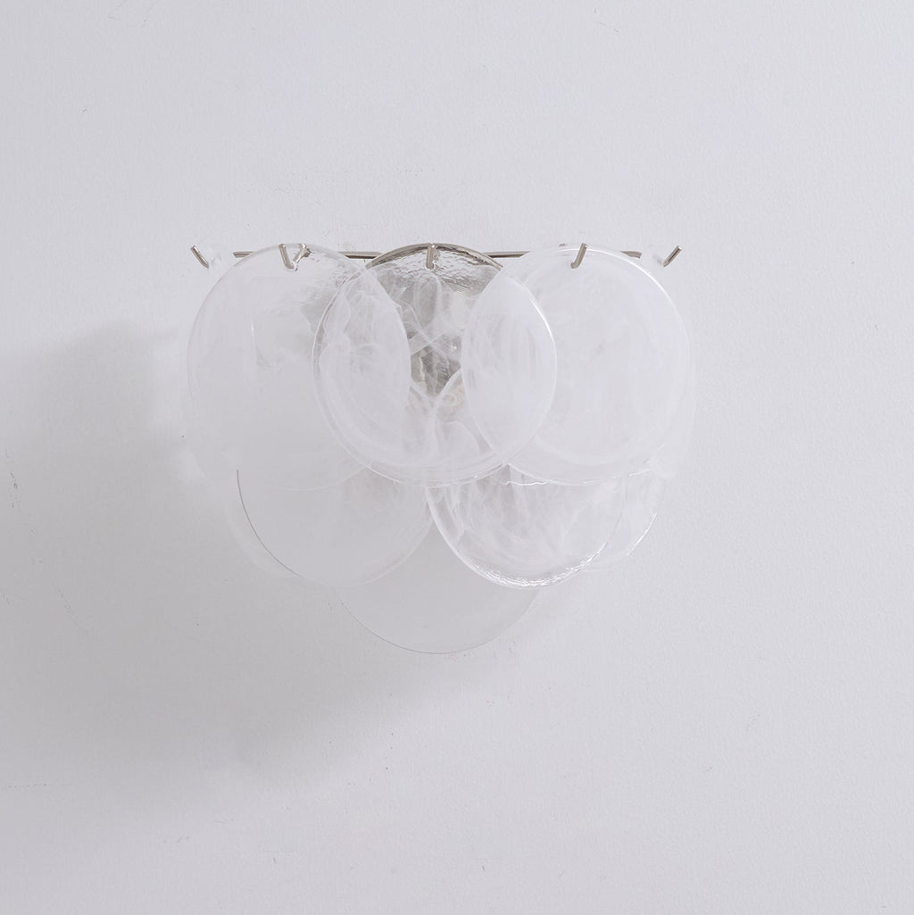 Unlit white glass-disc wall light from Clérachic with milky swirled discs on a plain pale wall, shown close up.