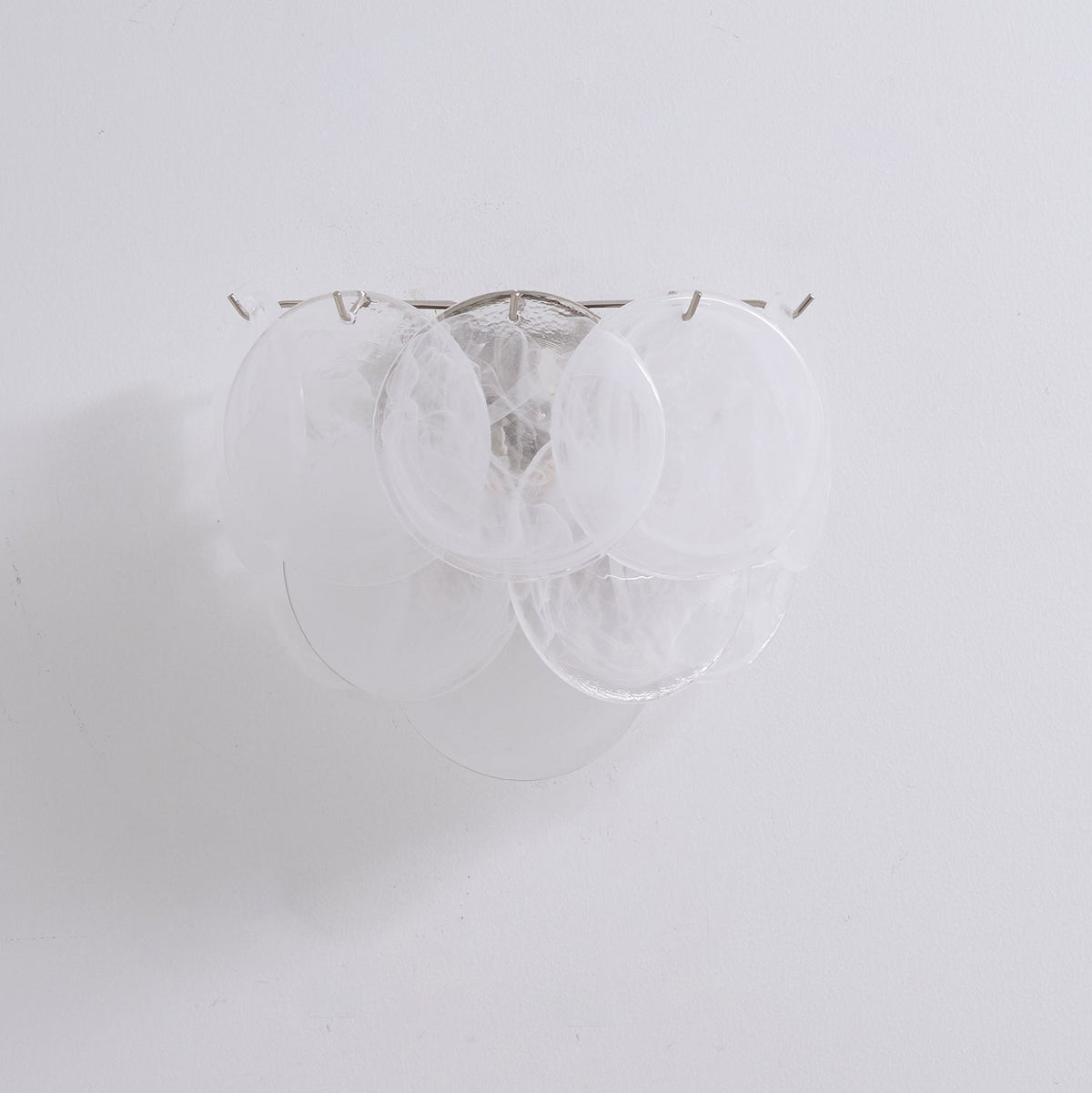 Unlit white glass-disc wall light from Clérachic with milky swirled discs on a plain pale wall, shown close up.