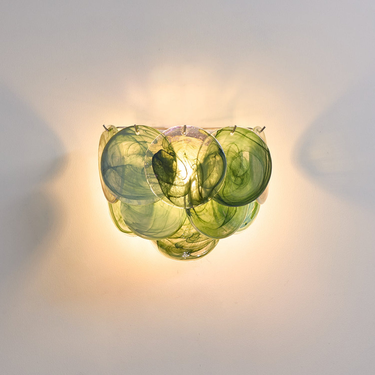 Close view of green swirled glass discs on this Clérachic wall light, lit warm so the layers glow yellow-green.
