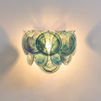 Close view of blue and teal swirled glass discs on this Clérachic wall light, lit warm against a pale wall.