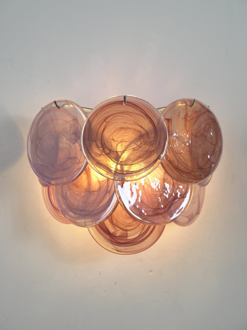 Pink and mauve swirled-glass wall light from Clérachic lit and angled slightly, with a warm glow behind the overlapping discs.