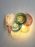 Side-on view of a lit multicolour wall light from Clérachic, with green, white, amber and rose discs layered together.