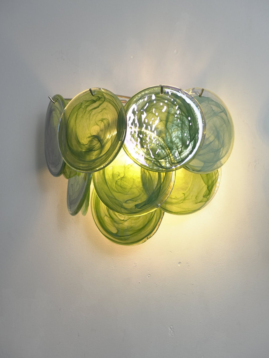 Lit green swirled-glass wall light from Clérachic shown at a slight angle, with olive and emerald discs glowing from within.