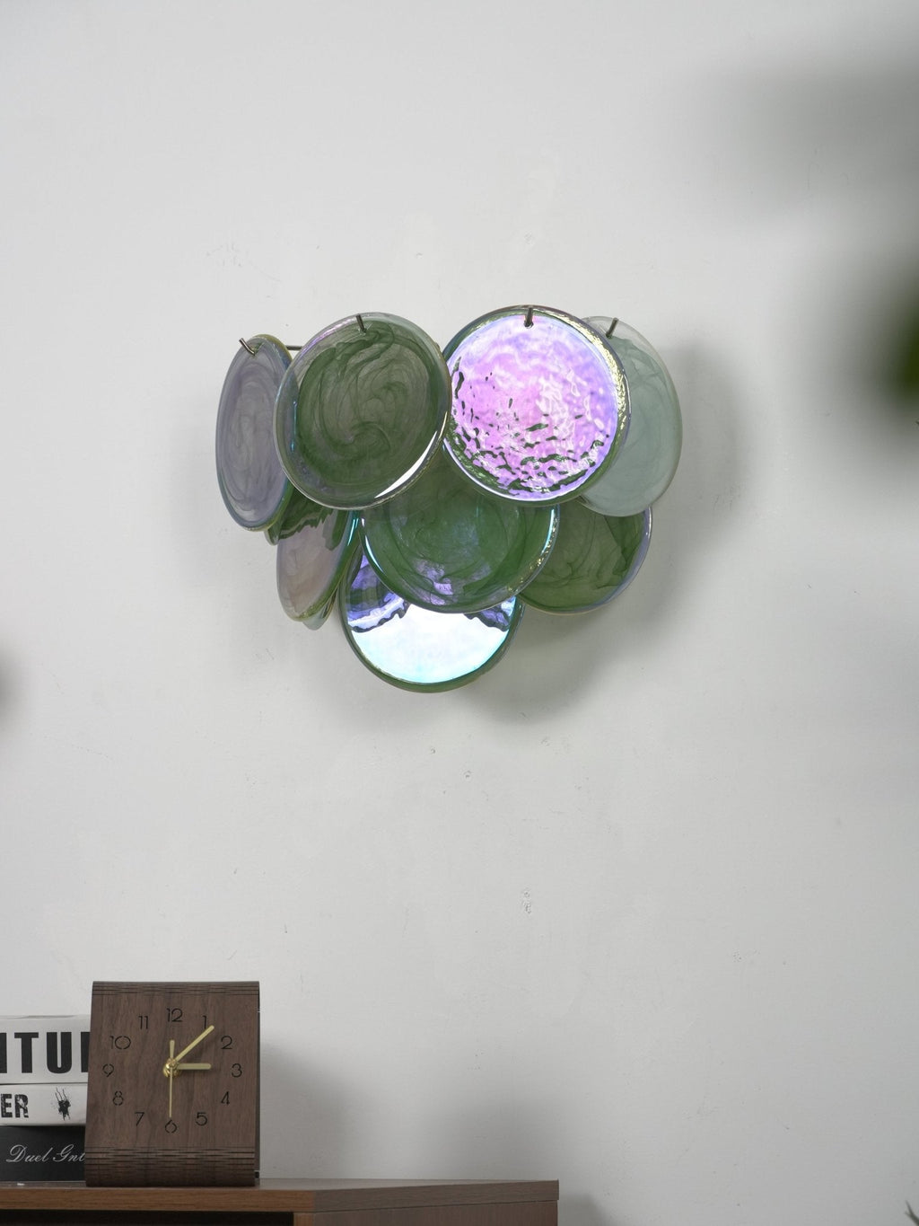 Unlit green glass-disc wall light from Clérachic with one iridescent pink-violet disc, above a cabinet with a desk clock.