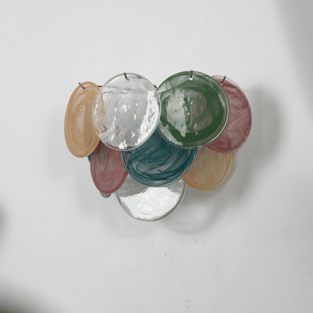 Unlit multicolour disc wall light from Clérachic in amber, clear, green, teal and rose glass, shown from the side on a grey wall.