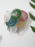 Multicolour disc wall light from Clérachic seen at an angle, with white, green, teal, rose and amber discs and a leaf at the edge.