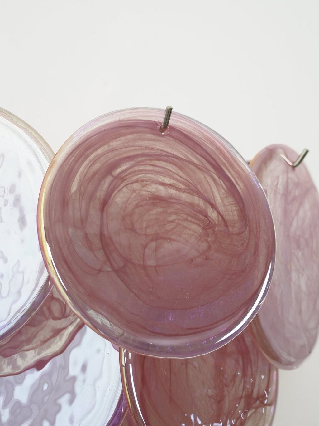 Close view of a swirled pink glass disc on this Clérachic wall light, showing its iridescent surface and the metal hook above.