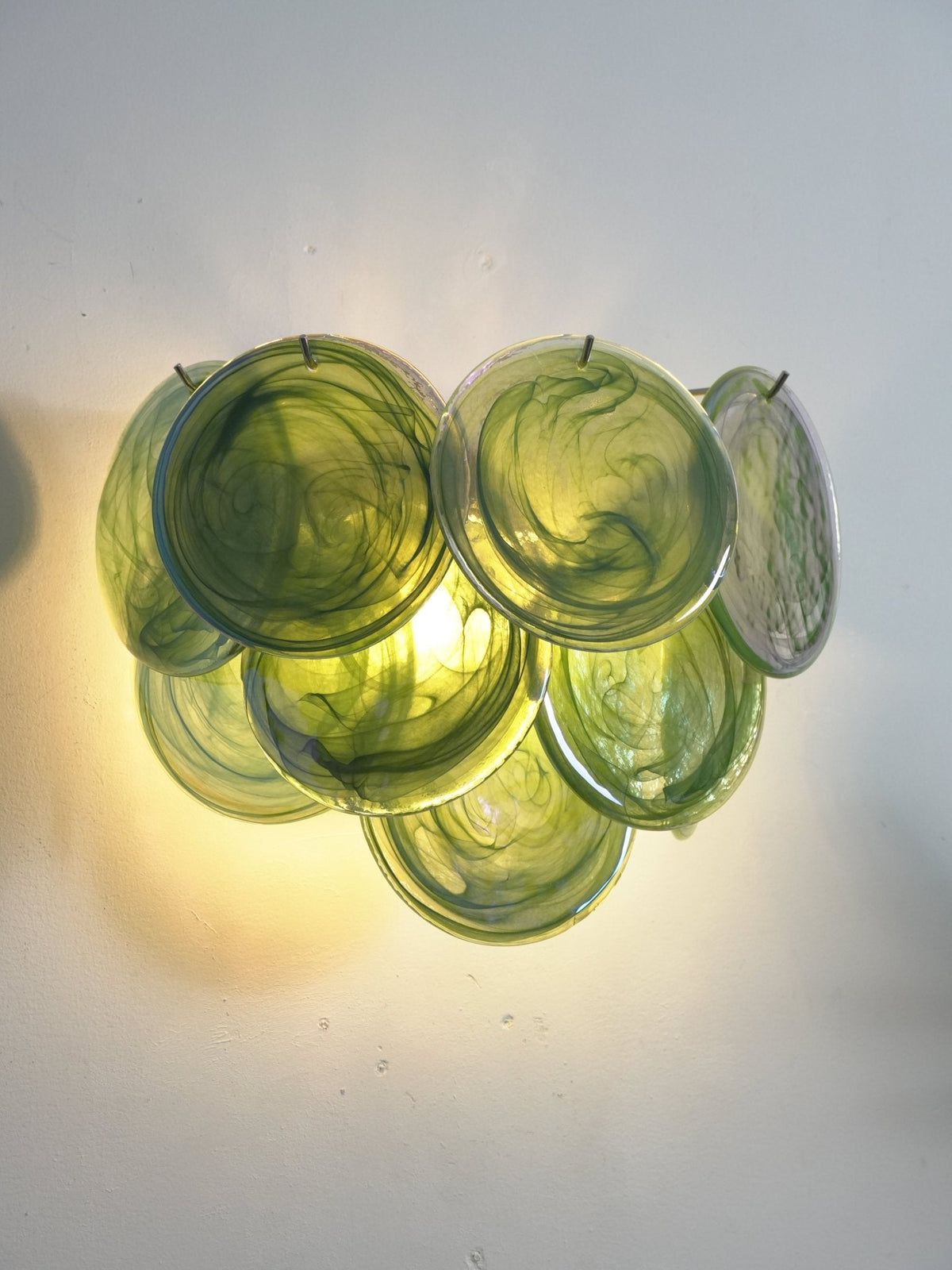 Close, lit view of green swirled glass discs on this Clérachic wall light, with a warm glow pooling on the wall beneath.