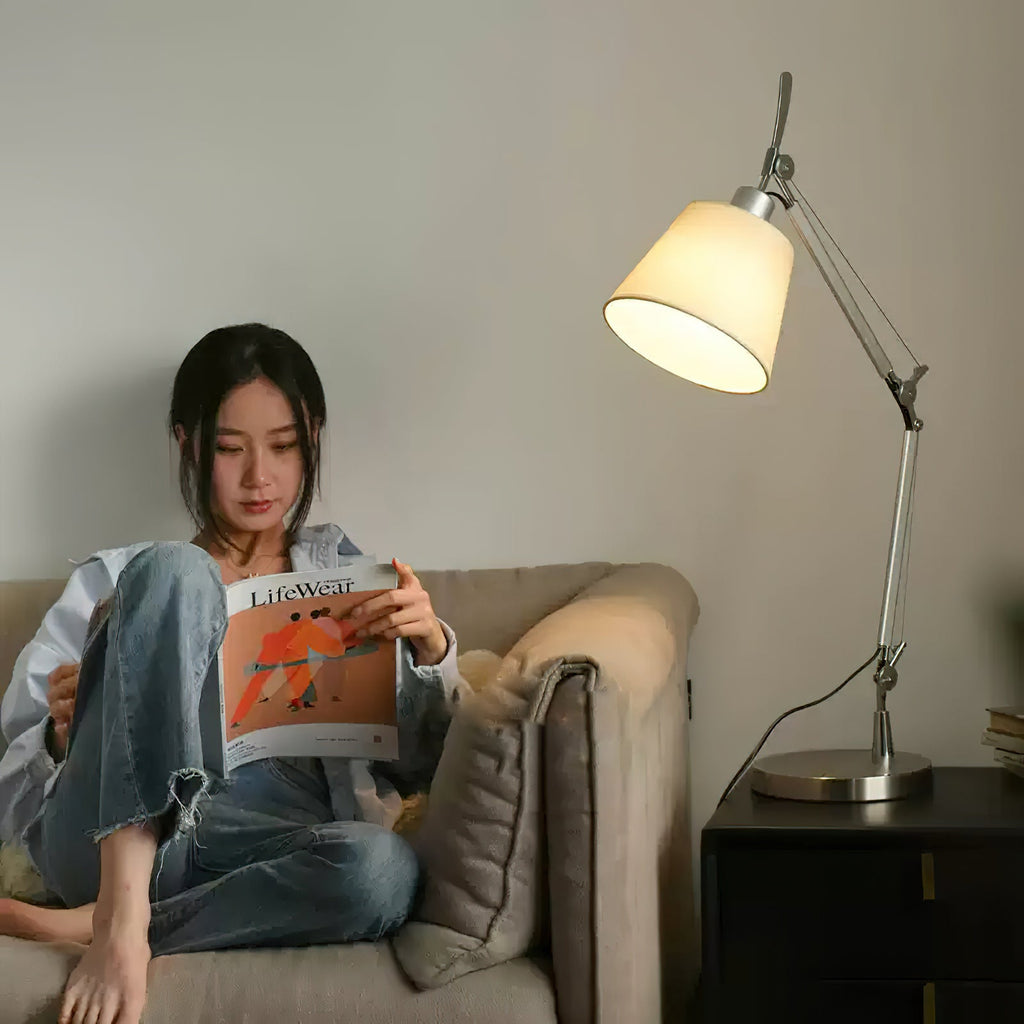 A woman reads a magazine on a beige sofa beside a black nightstand, with this Clérachic arm lamp glowing softly behind her.