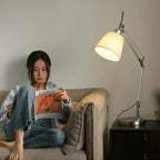 A woman reads a magazine on a beige sofa beside a black nightstand, with this Clérachic arm lamp glowing softly behind her.