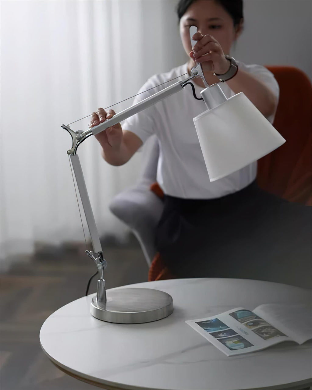Someone tilts the shade of this Clérachic swivel lamp on a round white table, with the arm bent at its joints.