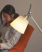 Close view of the warm glow from the white fabric shade of this Clérachic lamp, falling over a reader in an orange chair.