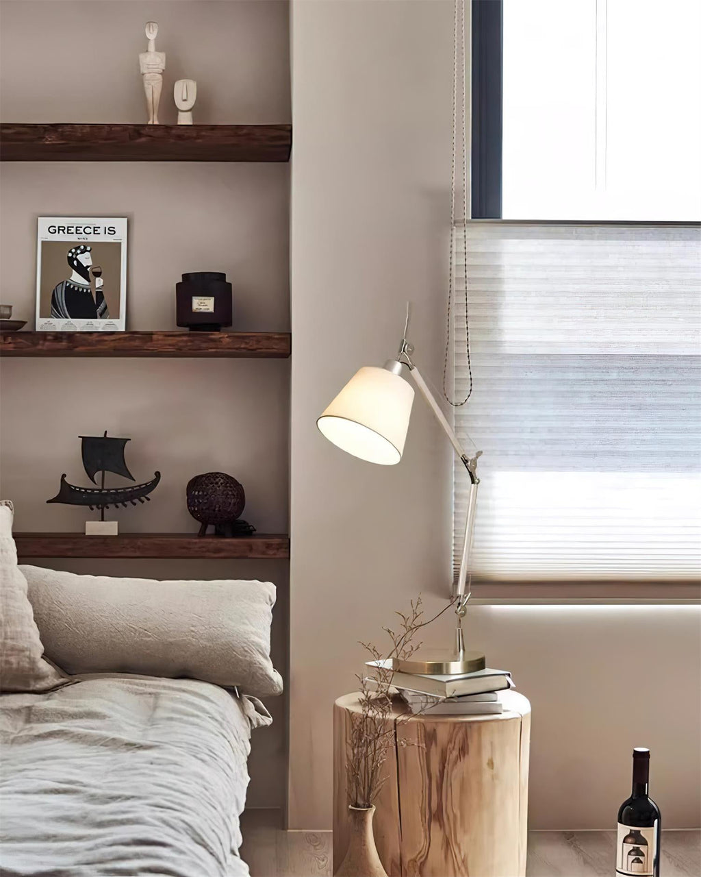 A Clérachic arm lamp lit beside a bed, with wooden shelves of small ornaments behind it and a log stool holding books.