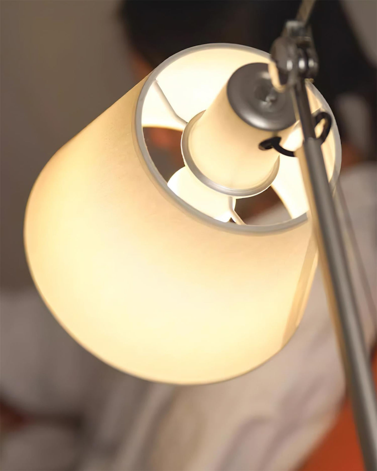 Close view of the lit white fabric shade and the silver bulb holder inside it on this Clérachic swivel lamp.