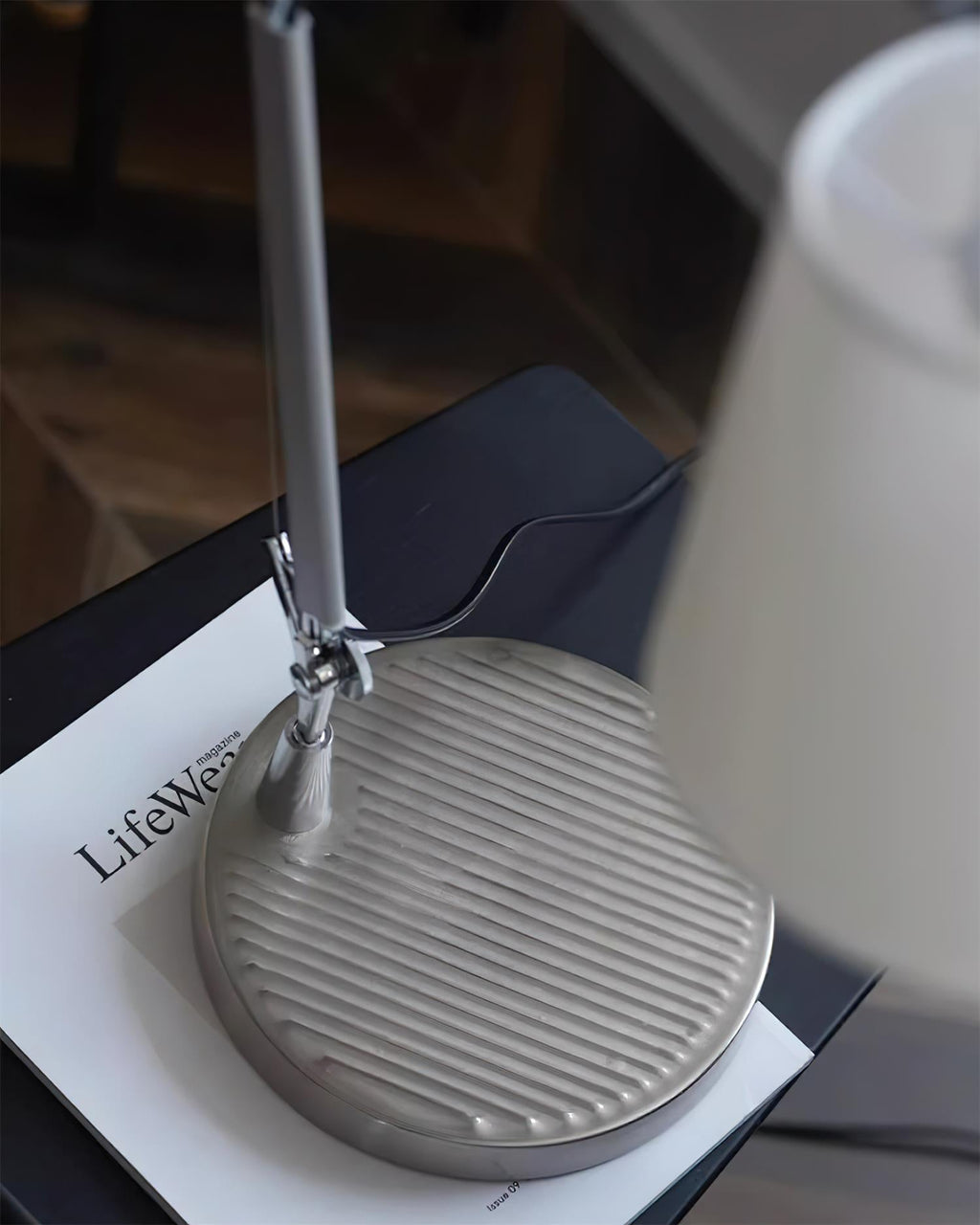 Close view of the round ridged metal base and the arm joint of this Clérachic table lamp, resting on a magazine.