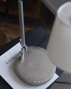 Close view of the round ridged metal base and the arm joint of this Clérachic table lamp, resting on a magazine.