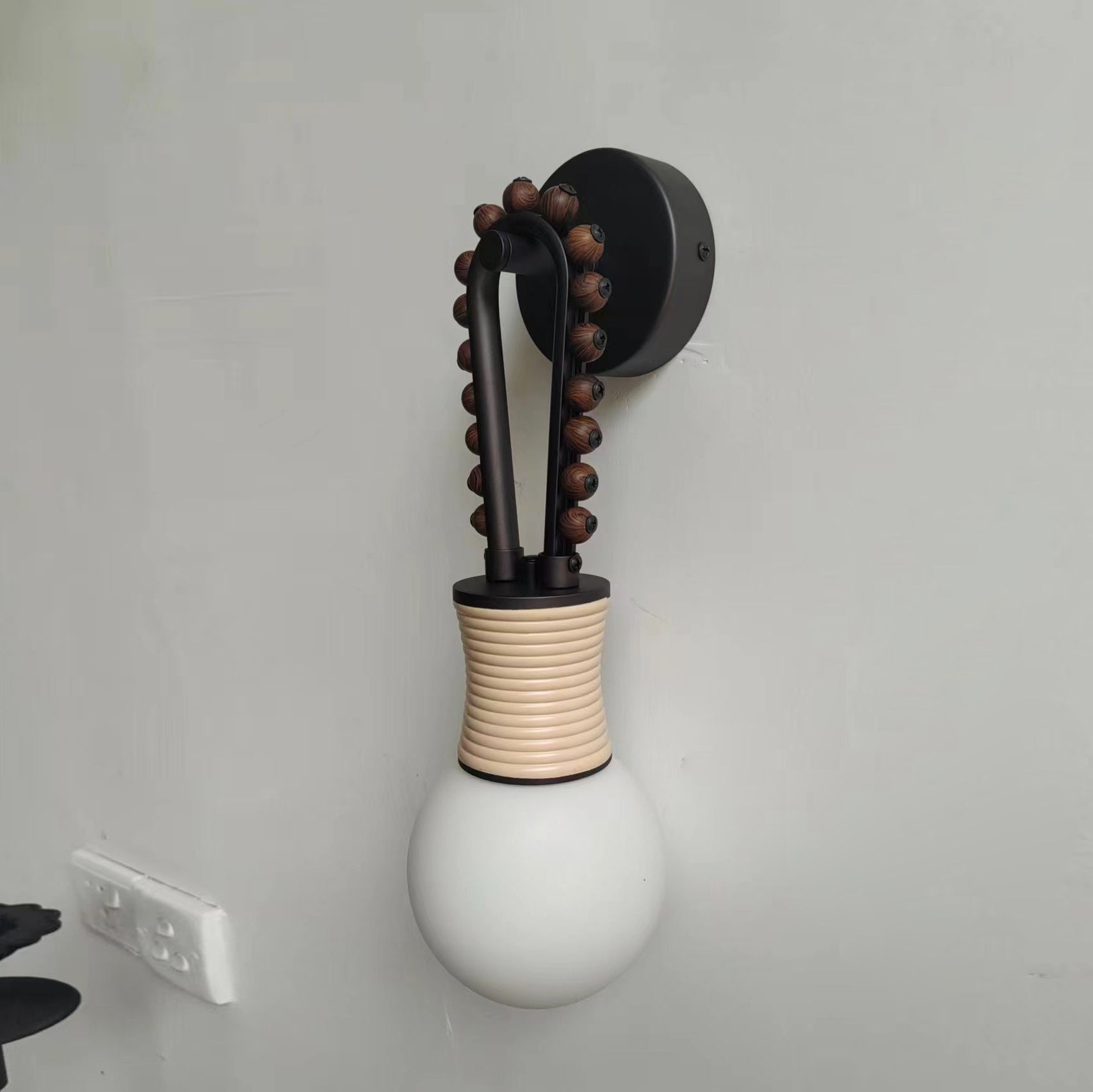 The Clérachic Sytala sconce mounted on a grey wall, showing its compact black backplate and bead arm.