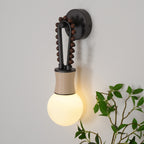 Clérachic Sytala sconce lit warm on a pale wall beside trailing greenery, opal globe glowing softly.