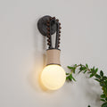 The Clérachic Sytala wall lamp glowing amber against off-white plaster, foliage curling in at the side.