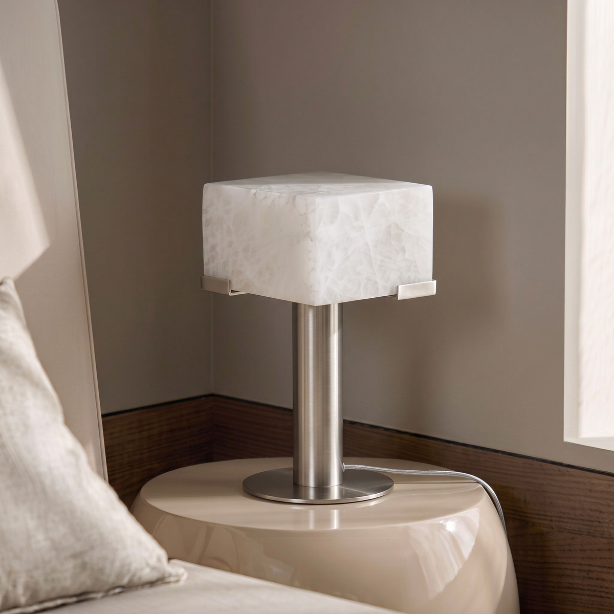 In nickel, this Clérachic table lamp stands on the same glossy cream nightstand beside a linen pillow.