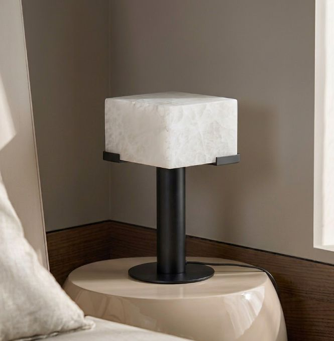 This Clérachic table lamp in matte black rests on a cream pedestal nightstand against a dark panelled wall.