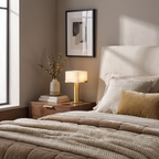 This brass Clérachic table lamp glows on a nightstand beside a bed with mustard and cream pillows.