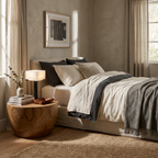Beside a bed with a charcoal throw, this black Clérachic table lamp sits lit on a round wood side table.