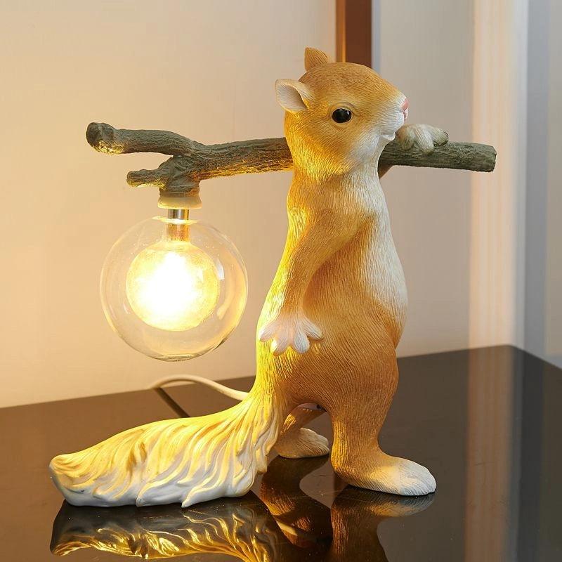 Lit Clérachic squirrel table lamp on a glossy black surface, its clear glass globe glowing warm from the end of the branch.