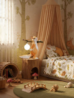 This Clérachic squirrel lamp lit beside a canopy bed in a child's room, on a tree-stump table with a toy bridge below.